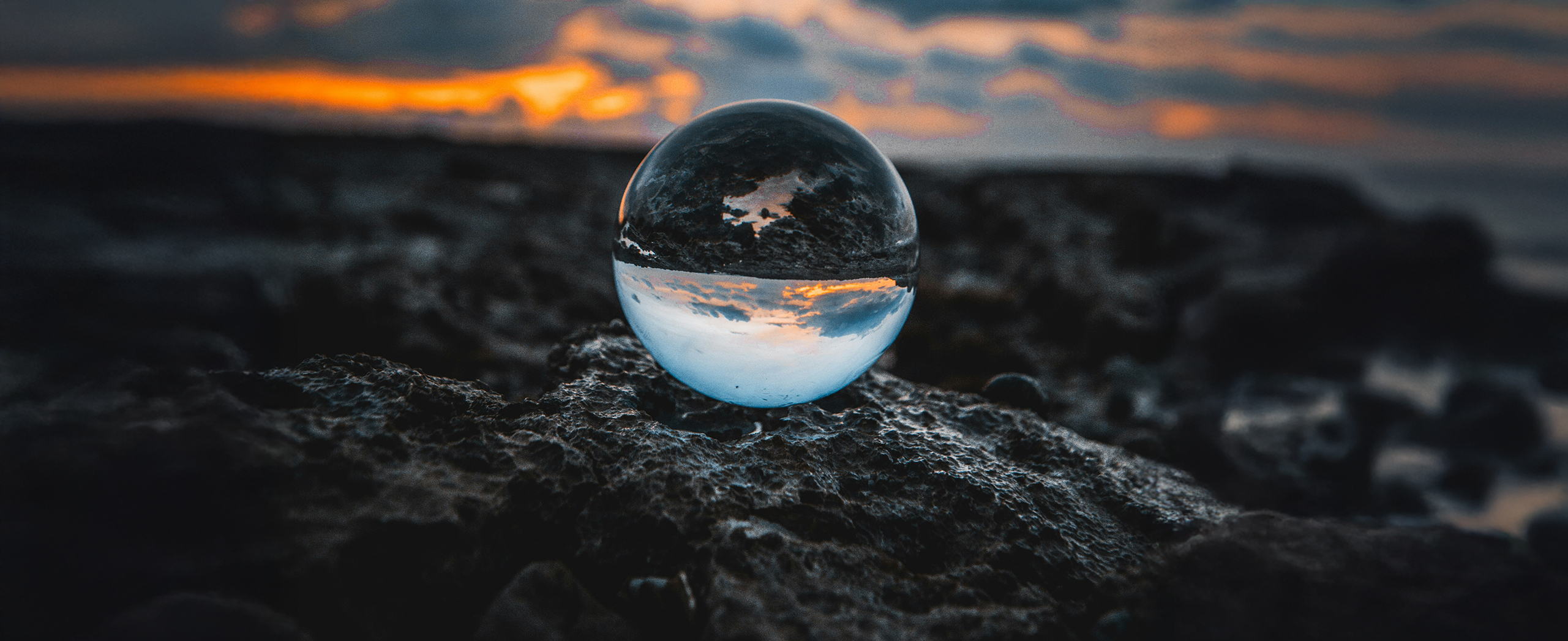 A clear sphere sitting on the shore showing a reflection of the ocean behind it.
