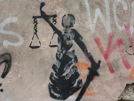 A spray-painted scales of justice surrounded by graffiti on a concrete wall.