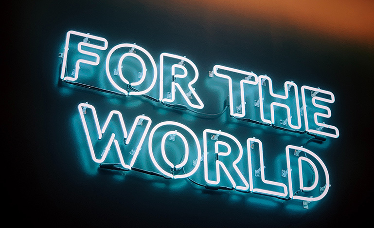 White neon sign with blue hue with the words "For the world"