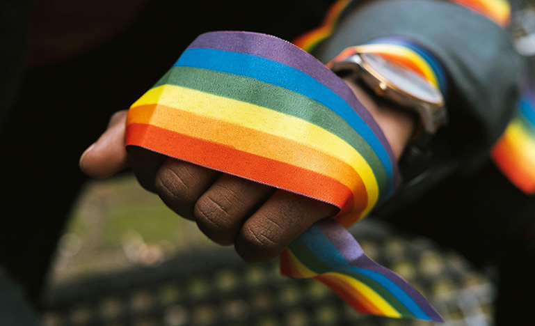 A ribbon with the pride flag colours wrapped around an outstretched hand.