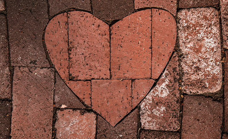 A dark brown brick wall with a heart made out of a light red bricks in the middle
