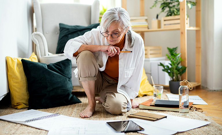 A senior person sitting on the floor surrounded by papers. 