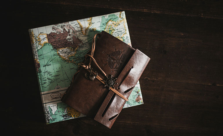 A leather-bound travel journal and a folded map sitting on top of a wooden table