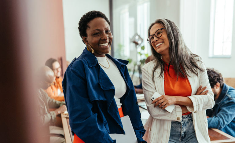 Two women standing next to each other, smiling. 