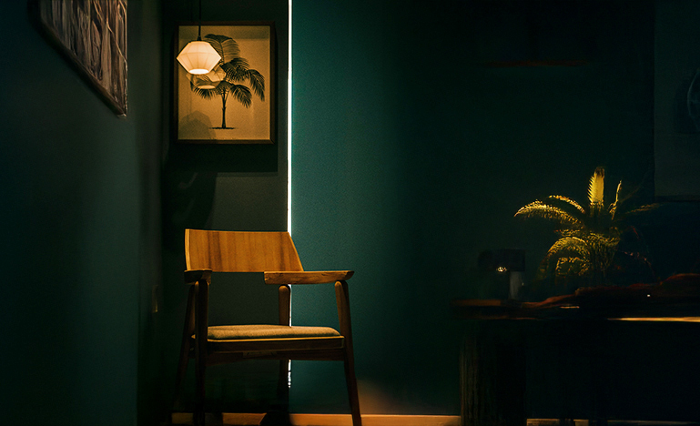 A chair in a dark corner with a light overhead.