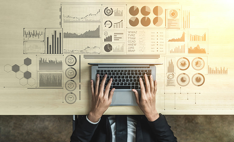 An aerial view of a person at a laptop surrounded by data charts. 
