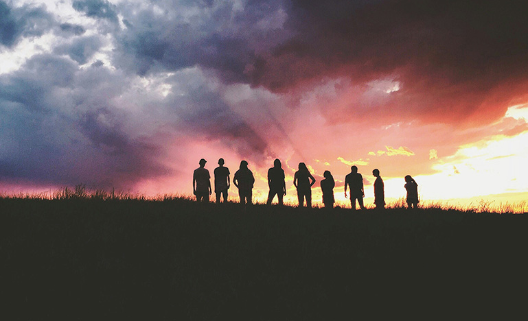 A group of young people standing on a hill at sunset.