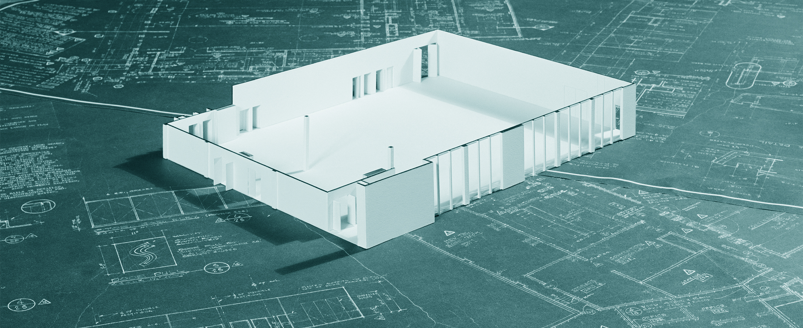 A model frame of a building sitting on a number of blueprints.