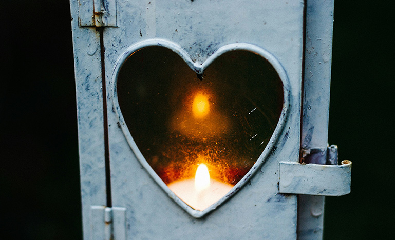 A candle burning behind a heart-shaped window