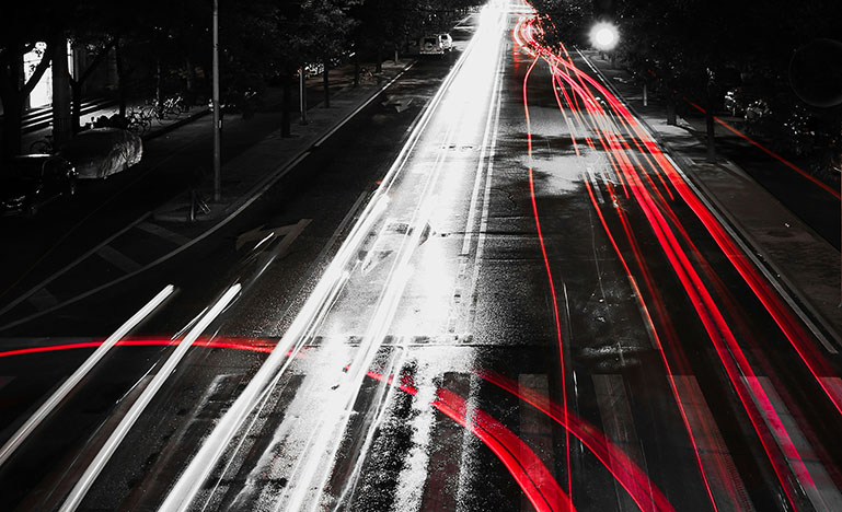 A street at night with car lights streaking up and down the road.