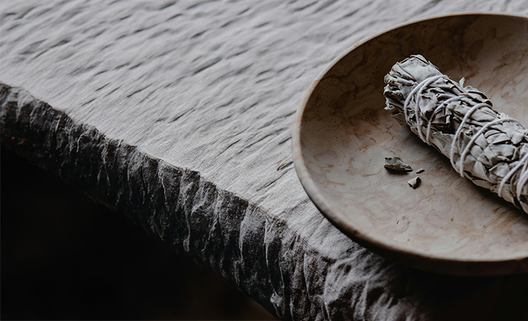 A bundle of sweetgrass in a wooden bowl sitting on a rough carved table.