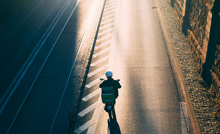 A delivery person riding a scooter as the sun starts to set