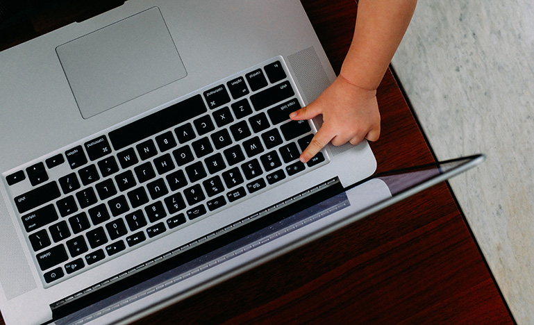 A small child trying to press a button on an open laptop