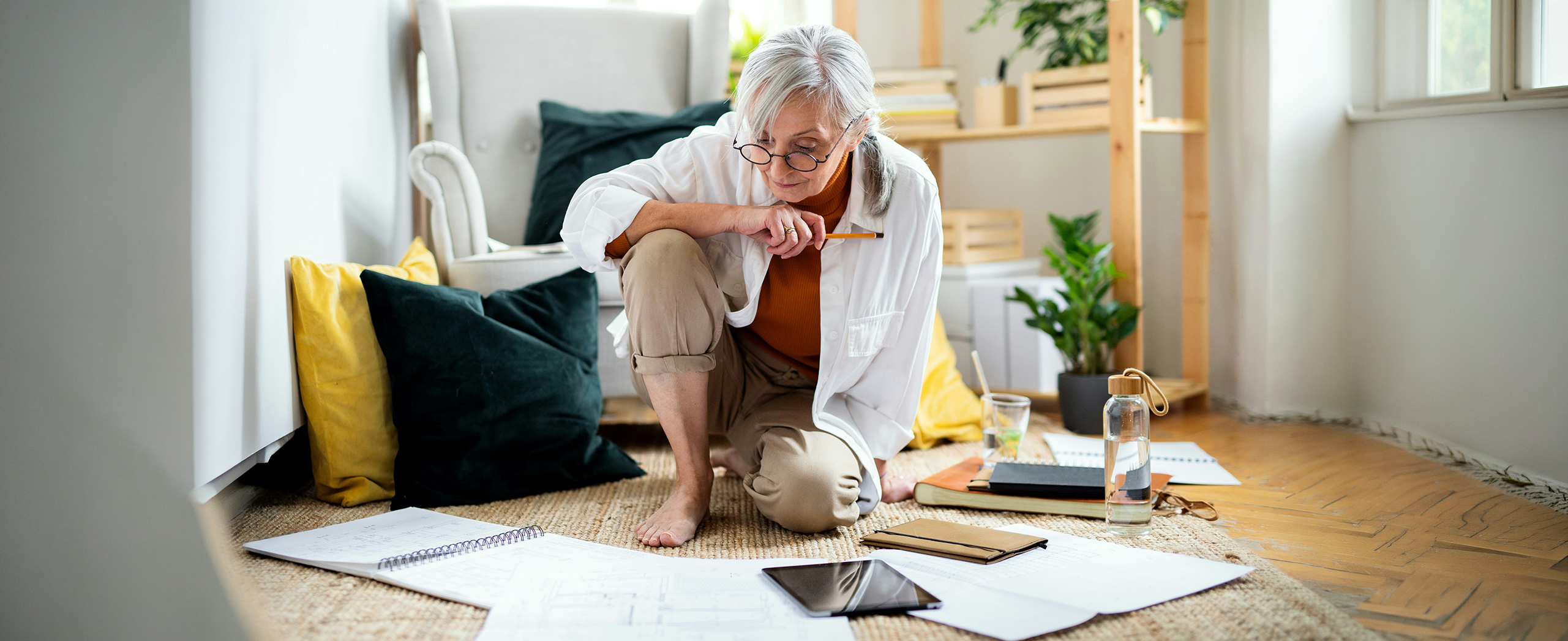 A senior person sitting on the floor surrounded by papers. 