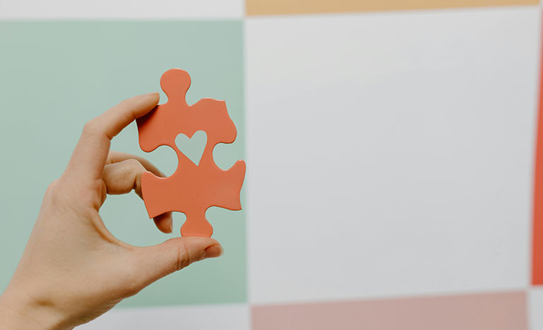 A hand holding a puzzle piece with a heart in the middle