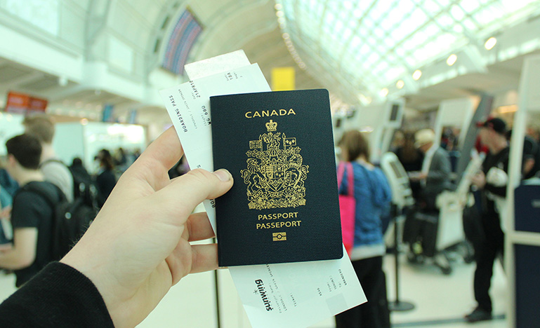 A person in an airport holding up a Canadian passport.