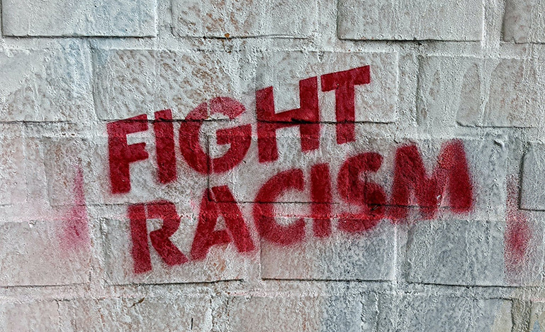 "Fight Racism" in red spray paint on grey brick wall