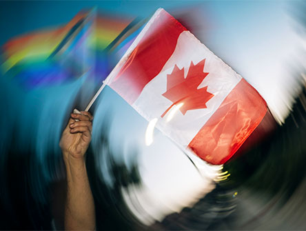 A person waving a Canadian flag and two inclusive Pride flags. 
