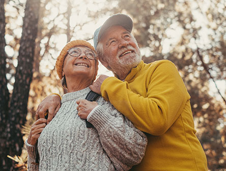 A senior couple embracing in a forest setting.