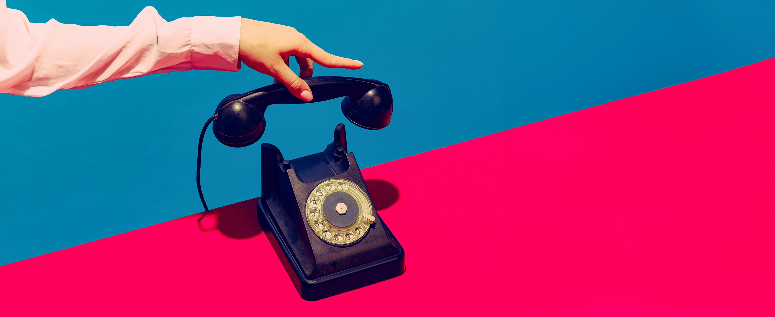 A hand holding the receiver of a vintage rotary phone. 